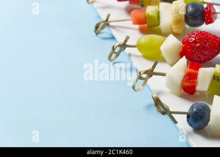 Crostini di frutta. Tartine di frutta fresca su piatto bianco. Frutta mista in piatto bianco stile alimentare sano, sfondi blu. Foto Stock
