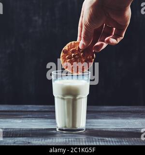 Womans dunking mano un cookie fatti in casa in un bicchiere di latte su uno sfondo nero. Foto Stock