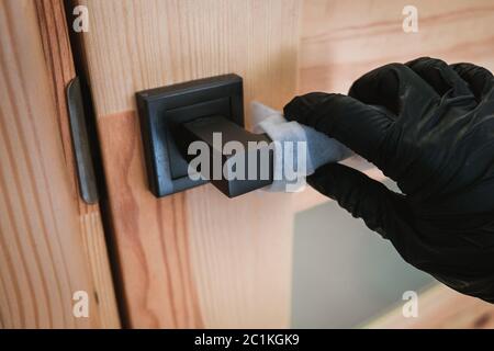 Aprire una porta di legno con guanti neri usando un tovagliolo. Protezione automatica durante l'isolamento dell'epidemia di virus. Misure di sicurezza personale per prevenire i virus Foto Stock