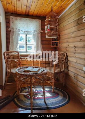 Soggiorno soleggiato in colori caldi con comoda poltrona e sgabello in vimini, armadio d'epoca, piante e grandi finestre Foto Stock
