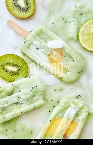 Gelato fatto in casa su un bastone con un pezzo di pesca. Pattern da spruzzi di pezzi di frutta diversa, ghiaccio e ghiaccio fondente cr Foto Stock