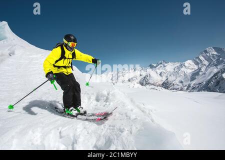 Sciatore professionista alla velocità prima di saltare dal ghiacciaio in inverno contro il cielo blu e le montagne Foto Stock