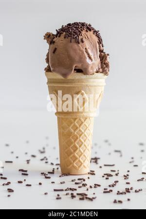 Gelato a fondo piatto singolo cono su sfondo bianco. Gelato al cioccolato con spruzzette Foto Stock