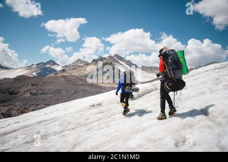 Due turisti, un uomo e una donna con zaini e ramponi sui loro piedi camminano lungo il ghiacciaio sullo sfondo della m Foto Stock