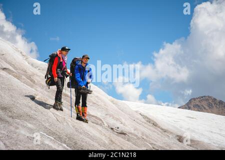 Due turisti, un uomo e una donna con zaini e gatti sui loro piedi, si trovano sul ghiaccio sullo sfondo delle montagne di Th Foto Stock