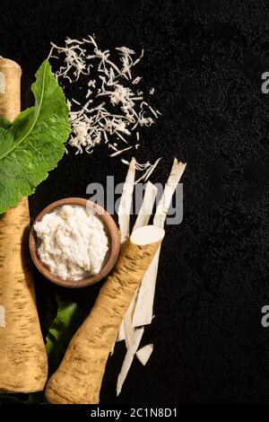 Radici di rafano grattugiate fresche su nero. Foto Stock