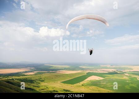 Un parapendio bianco-arancio vola sul terreno montuoso Foto Stock