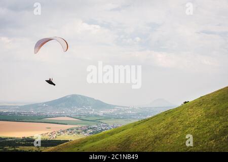 Un parapendio bianco-arancio vola sul terreno montuoso Foto Stock