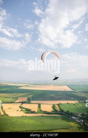 Un parapendio bianco-arancio vola sul terreno montuoso Foto Stock