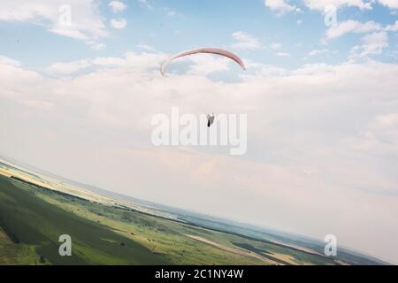 Un parapendio bianco-arancio vola sul terreno montuoso Foto Stock