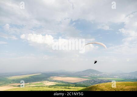 Un parapendio bianco-arancio vola sul terreno montuoso Foto Stock