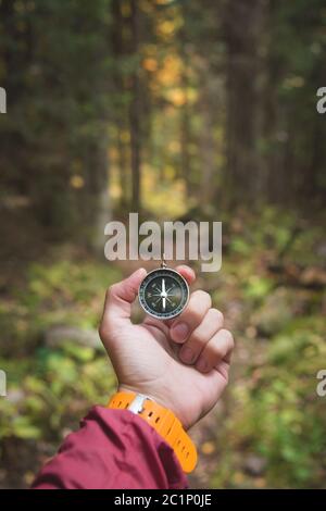 Una bella mano maschile con una cinghia gialla per orologio tiene una bussola magnetica nella foresta di conifere autunno. Il concetto di trovare Foto Stock