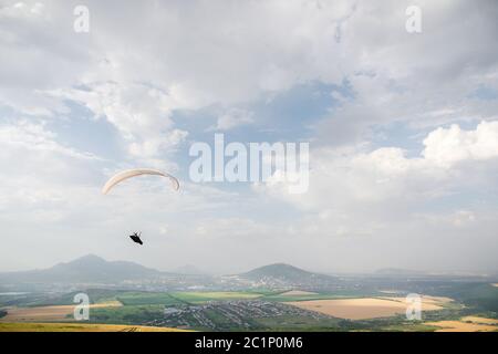 Un parapendio bianco-arancio vola sul terreno montuoso Foto Stock