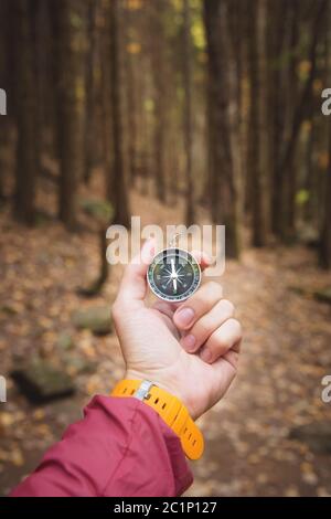 Una bella mano maschile con una cinghia gialla per orologio tiene una bussola magnetica nella foresta di conifere autunno. Il concetto di trovare Foto Stock