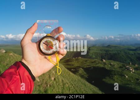 Uomo alla ricerca di direzione con una bussola in mano nel punto di vista estivo delle montagne. Ricerca direzione Foto Stock