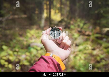 Una bella mano maschile con una cinghia gialla per orologio tiene una bussola magnetica nella foresta di conifere autunno. Il concetto di trovare Foto Stock