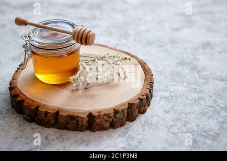 Il vasetto di vetro pieno di miele fresco posto sulla fetta di legno Foto Stock