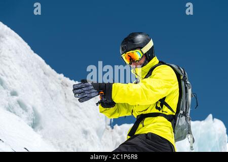 Lo sciatore professionista in un casco con uno zaino e una maschera da sci in piedi su un ghiacciaio si prepara a saltare indossando guanti a membrana Foto Stock