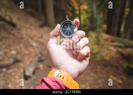 Una bella mano maschile con una cinghia gialla per orologio tiene una bussola magnetica nella foresta di conifere autunno. Il concetto di trovare Foto Stock