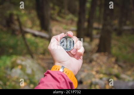 Una bella mano maschile con una cinghia gialla per orologio tiene una bussola magnetica nella foresta di conifere autunno. Il concetto di trovare Foto Stock