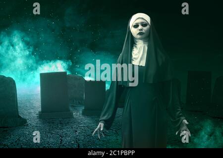 Terrificante suora del diavolo in piedi con fuoco mistico sul cimitero. Concetto di Halloween Foto Stock