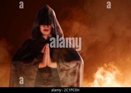 Donna strega asiatica con mantello nero che fa rituale mistico con sfondo di fumo Foto Stock