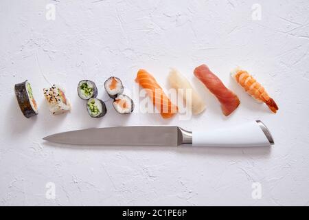 Vari rotoli di sushi con coltello giapponese sulla pietra bianca di sfondo di ardesia Foto Stock