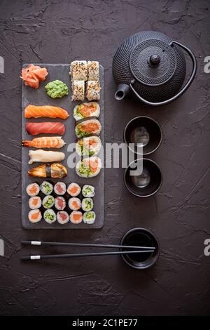 Assortimento di tipi differenti di sushi rotoli posti sulla pietra nera board Foto Stock