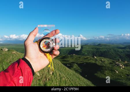 Uomo alla ricerca di direzione con una bussola in mano nel punto di vista estivo delle montagne. Ricerca direzione Foto Stock