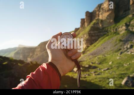 Uomo alla ricerca di direzione con una bussola in mano nel punto di vista estivo delle montagne. Ricerca direzione Foto Stock