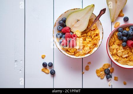 Golden corn flakes con frutti freschi di lamponi mirtilli e pera in vaso in ceramica Foto Stock