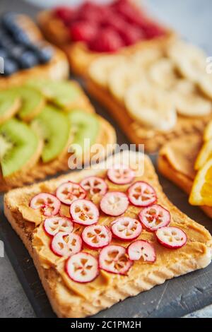 Sei fette biscottate con burro di arachidi, frutta fresca su un livello di grigio ardesia Foto Stock