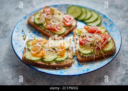 Piastra con toast con cucomber, pomodori e feta sbriciolata e germogli di rafano Foto Stock