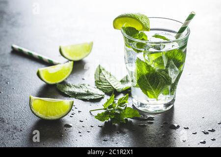 Cocktail con cubetti di lime, menta e ghiaccio su tavolo nero. Foto Stock