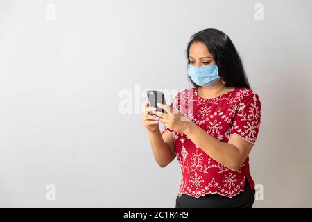 Una signora indiana tiene il suo telefono mentre indossa una maschera a casa Foto Stock
