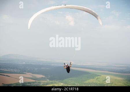 Il parapendio professionista in tuta di cocco vola in alto sopra il terreno contro il cielo e i campi Foto Stock