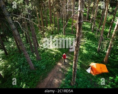 Vista aerea dell'uomo che cammina vicino alla tenda arancione nella foresta in montagna. Foto scattata con il drone Foto Stock