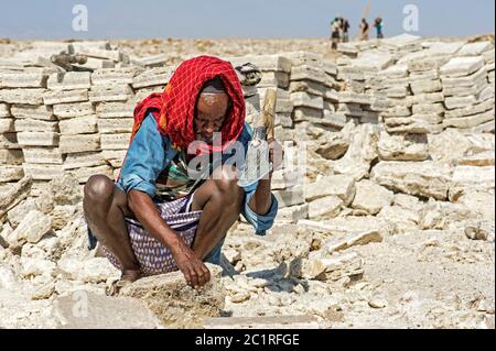 Uomo locale taglio blocchi di sale in una cava di sale al lago salato Assale, Hamedala, Danakil depressione, Afar Regione, Etiopia Foto Stock