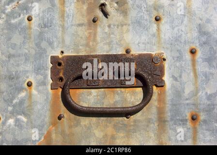 Maniglia arrugginita su vecchia porta rivestita con chiodatura zincata lamiera in Sicilia Foto Stock