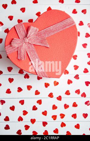 Regalo confezionato posto su a forma di cuore di paillettes rosso su bianco tavolo in legno Foto Stock