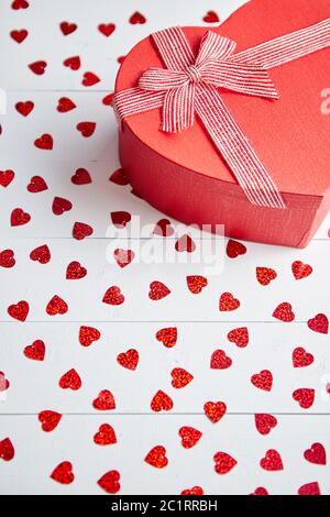 Regalo confezionato posto su a forma di cuore di paillettes rosso su bianco tavolo in legno Foto Stock