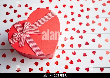 Regalo confezionato posto su a forma di cuore di paillettes rosso su bianco tavolo in legno Foto Stock