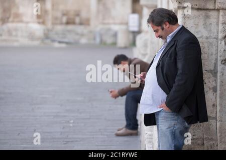 Due italiani impegnati con il loro smartphone sulla piazza del Popolo di Ascoli Piceno, Italia Foto Stock