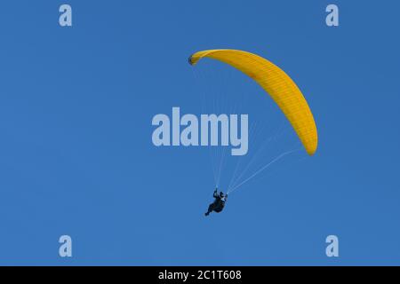 Il pilota di parapendio con un aliante giallo sta volando nel cielo azzurro, sport di avventura agonistico e ricreativo, copy space Foto Stock