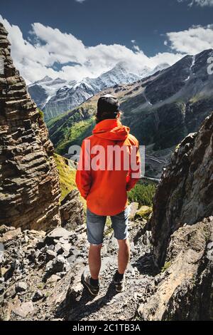 Ritratto di un escursionista maschile in pantaloncini e un cappello dal retro è in piedi su alte rocce al bordo di una scogliera contro lo sfondo Foto Stock