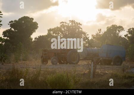 Un trattore rosso che trasporta macchinari agricoli, parcheggiando in un campo durante il tramonto Foto Stock