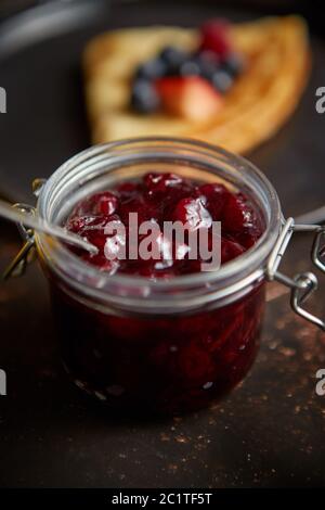 Vicino sul vaso riempito con fresca marmellata di ciliegia immessi sul buio tavolo arrugginita Foto Stock