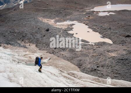 Un alpinista con uno zaino cammina in ramponi camminando lungo un ghiacciaio polveroso con marciapiedi tra le fessure nel Foto Stock