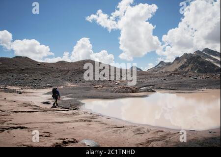 Un alpinista con uno zaino cammina in ramponi camminando lungo un ghiacciaio polveroso con marciapiedi tra le fessure nel Foto Stock