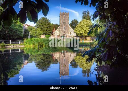 La pittoresca chiesa normanna di St Mary vista dall'altra parte dello stagno del villaggio a Buriton nel South Downs National Park, Hampshire, Inghilterra, Regno Unito Foto Stock